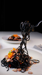 Eating spicy squid ink black spaghetti with shrimp ,ham ,bacon ,garlic ,chilli ,olive oil and mushroom on the plate decorated with basil leave. Mediterranean delicacy food.On white table