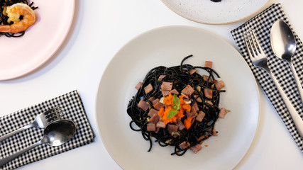 top view  of spicy squid ink black spaghetti with shrimp ,ham ,bacon ,garlic ,chilli ,olive oil and mushroom on the plate decorated with basil leave. Mediterranean delicacy food.On white table
