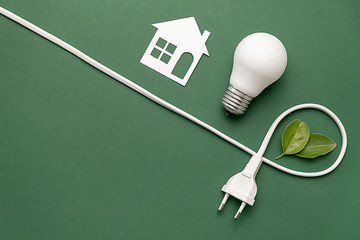 Flat lay top view of white paper house, LED light bulb, plug-like and fresh leaves on green...