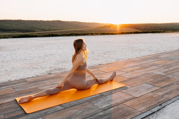 Young slim fit woman doing stretching exercise, twine pose, at the sunset. Yoga teacher outdoors.