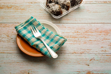 Fork on cloth on plate. Visible kaswi topped with grated coconut (brown steamed Malaysian dessert, rice, tapioca flour, white sugar, alkaline water and palm sugar combined.) Selective focus.