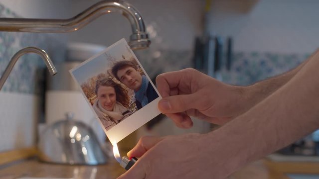 Close up male hands burning a family photo in the kitchen sink. Couple quarreled, divorce
