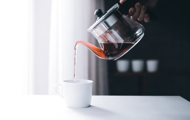 An anonymous hand is filling coffee to cup from a pot with copy space