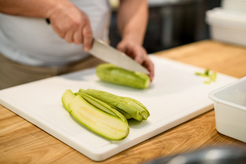chef cuts green zucchini with knife into pieces.