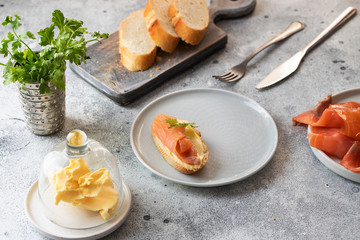Bruschetta with smoked salmon and butter on concrete table with bread, butter and herbs. Delicious snack or appetizer.