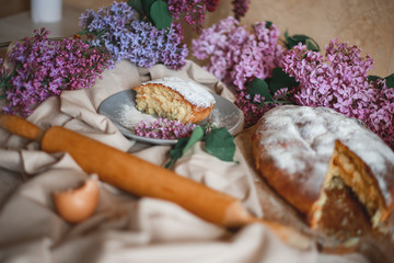 Obraz na płótnie Canvas Homemade Apple pie on a wooden table next to a bowl of lilacs. Gentle toning.
