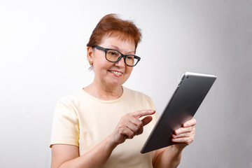Senior woman in glasses uses a tablet on a white background in a light T-shirt. place for text, isolated