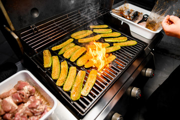 Zucchini slices spread on grill grid and fried on fire.