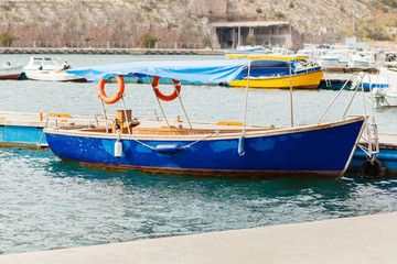 Naklejka na ściany i meble old boat near a pier the sea. Old Harbour With Fishing Boats. Yacht On The Marina Dock. Old harbour in the mediterranean sea with small fishing boats. Landscape View Of Water Near Beach. local tourism