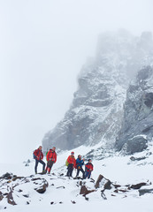 Male tourists with backpacks and trekking sticks taking break during hike in winter mountains....