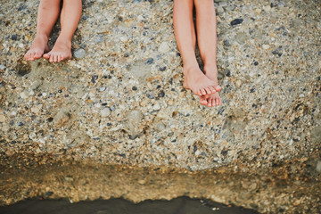 Children's feet sitting on a stone.