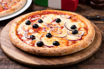 Pizza with onions and black olives on the wooden board.