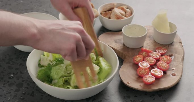 Man hand mix romaine lettuce and dressing to make caesar salad in white ceramic bowl on concrete countertop