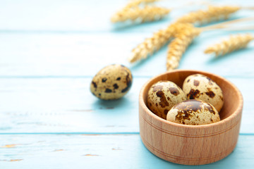 Fototapeta na wymiar Quail eggs with spikelets of wheat on blue wooden background. Top view. Free space.