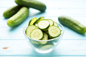 Fresh cucumber slices in bowl on blue wooden background.