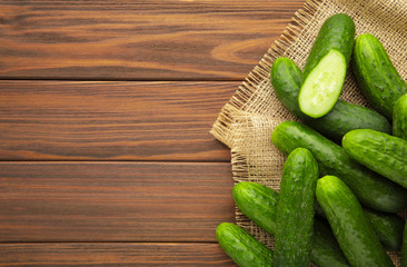 Fresh cucumbers with sackcloth on brown wooden background