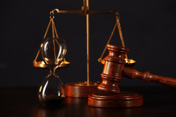 Law and justice concept. Lawyers desk. Judge's gavel, scales, hourglass, wooden table. Dark gray bokeh background