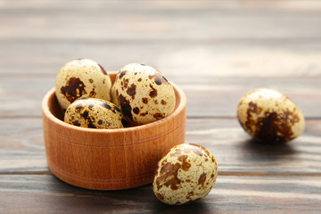 Fresh quail eggs in bowl on brown wooden background