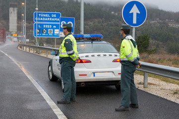 Guardia Civil officers next to his car watch traffic on a highway on a rainy day