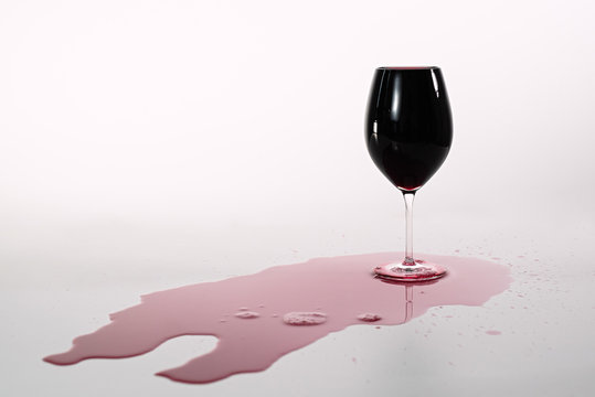 the glass with red wine is full, the wine is poured on a white table, the full glass of red wine is poured on the table, alcohol, red juice,