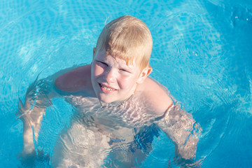 a disgruntled boy is sitting in the pool. a blond little hero gets angry at his parents while swimming in an outdoor pool. Child having fun in swimming pool.