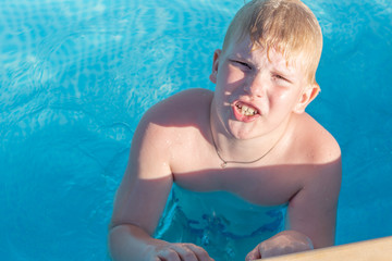 a disgruntled boy is sitting in the pool. a blond little hero gets angry at his parents while swimming in an outdoor pool. Child having fun in swimming pool.