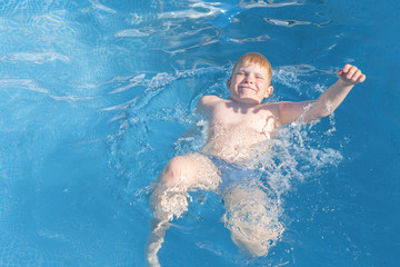 a very strong boy swims on his back. funny blond kid having fun in the outdoor pool in the bright sun