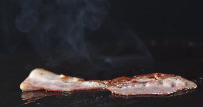 A piece of bacon in a frying pan with hot steam.