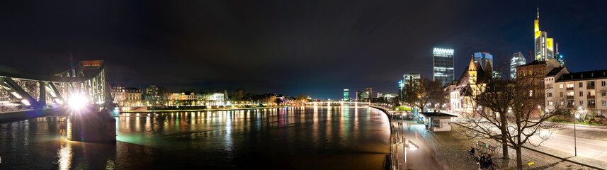 Night view from the Eisenerner Steg bridge over the Main river to the illuminated cityscape of Frankfurt