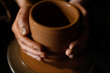 The potter's hand in the product formed on a potter's wheel. Red clay turns into a cup.