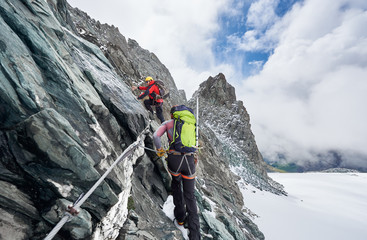 Back view of rock climbers with backpacks using fixed rope while ascending high rocky mountain. Male mountaineers climbing natural rock formation and trying to reach mountaintop.