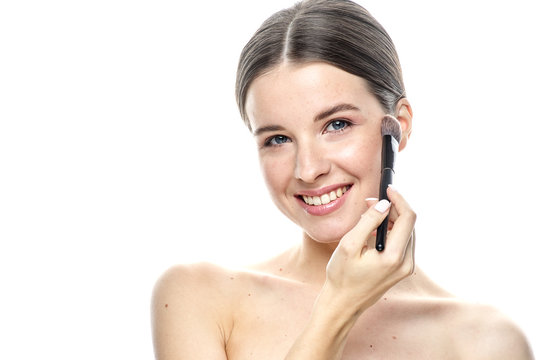 close-up portrait of a young brunette girl with blue eyes with clear skin, doing makeup with makeup brushes, isolated on a white background. High-resolution photos
