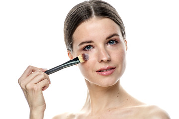 close-up portrait of a young brunette girl with blue eyes with clear skin, doing makeup with makeup brushes, isolated on a white background. High-resolution photos