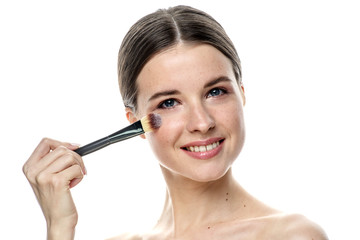 Obraz na płótnie Canvas close-up portrait of a young brunette girl with blue eyes with clear skin, doing makeup with makeup brushes, isolated on a white background. High-resolution photos