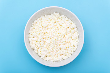 Fresh cottage cheese in a white bowl on a blue background. Milk curd on a plate. Top view. 