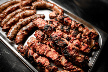 Close-up of metal tray with ready-made grilled pieces of beef meat.
