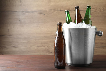 Metal bucket with beer and ice cubes on wooden table. Space for text