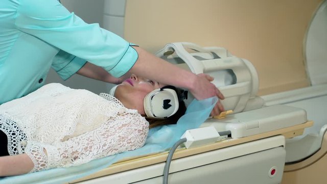 Female patient lays in a MRI scanner. Nurse prepares the patient before making tomographic scanning. Modern medical equipment in clinic.
