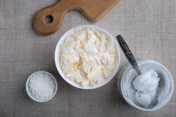 Bowl of coconut flakes and jar of coconut oil on fabric background. Superfoods. Top view.