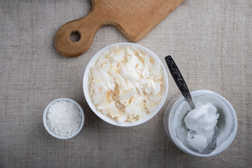 Bowl of coconut flakes and jar of coconut oil on fabric background. Superfoods. Top view.