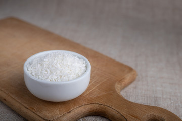Coconut flakes in a bowl on a wooden board on the table