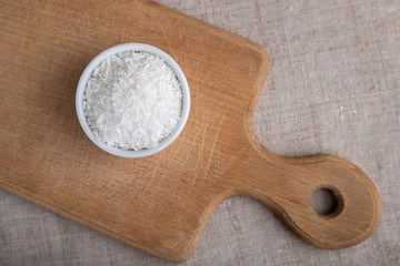 Coconut shavings in a bowl on a wooden board on the table