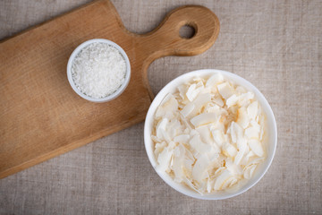 Coconut chips and shavings in a bowl on a cloth tablecloth and cutting board.Top view.