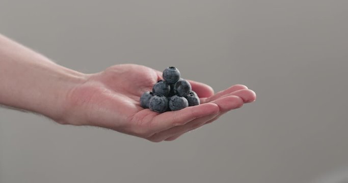 Slow motion man hand show big ripe blueberries on neutral background
