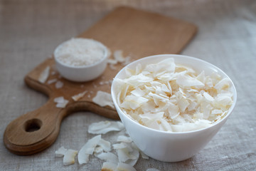 Coconut chips and shavings in a bowl on a cloth tablecloth and cutting board