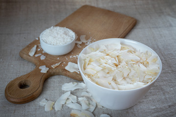 Coconut chips and shavings in a bowl on a cloth tablecloth and cutting board