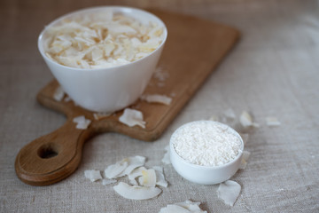Coconut chips and shavings in a bowl on a cloth tablecloth and cutting board