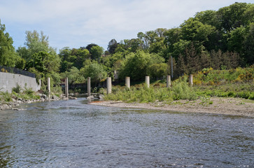 A view of an unfinished bridge on the River Dargle in Bray, Co. Wicklow, Ireland. Row of concrete columns located across the river. Abandoned structure.