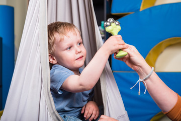 Pediatric Sensory Integration Therapy - boy swinging and playing a musical instrument - obrazy, fototapety, plakaty
