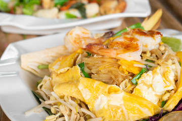 Omelet wraped Pad Thai with fresh shrimp in white dish on bamboo table, Fried white noodle.